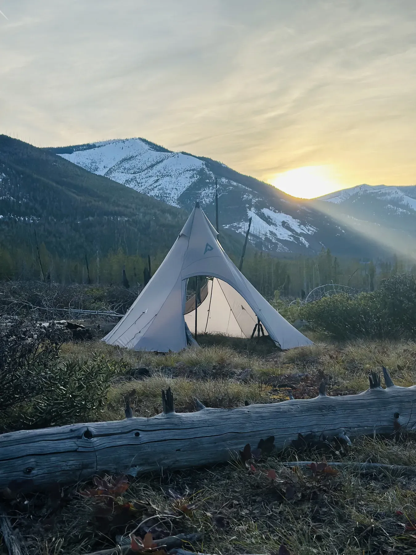 A tent pitched below snow-capped peaks at sunset